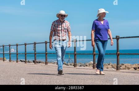 Ein Paar schlendern entlang der Esplanade in Sidmouth und genießen die heiße Sonne vor dem Feiertagswochenende. Quelle: DWR Stockfoto