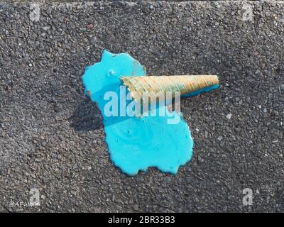 Ein Waffelcroissant mit türkisfarbenem Eis ist auf den dunkelgrauen Betonboden gefallen und ist flüssig geworden und durchgesickert. Nahaufnahme in zwei kontrastierenden c Stockfoto