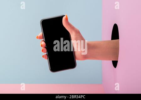 Nahaufnahme der Hand einer Frau, die ein Telefon auf blauem und rosa Hintergrund hält Stockfoto