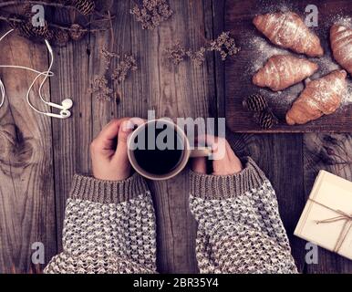 Keramik braun Tasse mit schwarzem Kaffee und Holz Schneidebrett mit gebackenen Croissants, gebacken mit Puderzucker, Hände halten einen Becher Stockfoto