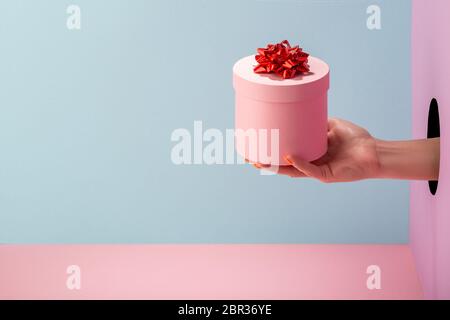 Hand der Frau hält eine runde Geschenkbox auf blauem und rosa Hintergrund Stockfoto