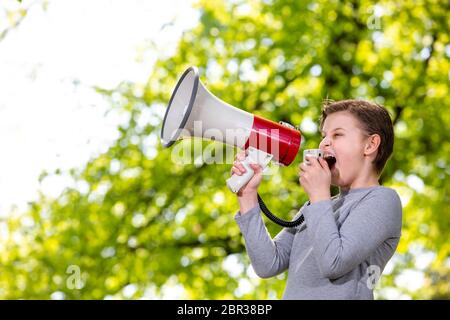 Ankündigendes Konzept, Junge schreiend oder schreiend durch das Megaphon über Wald Hintergrund mit Copyspace Stockfoto