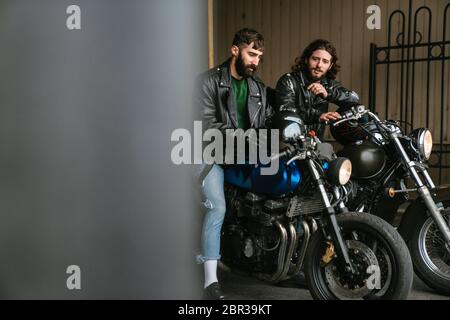 Foto von bärtigen kaukasischen Männern Biker sprechen, während sie auf ihren Fahrrädern in der Stadt sitzen Stockfoto