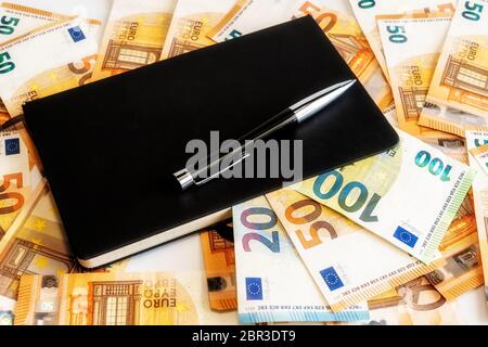 Schwarzer Rollstift auf einem schwarz karierten Notizbuch. Mani Euro Banknote auf Hintergrund. Geschäftskonzept. Stockfoto