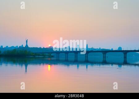 Anzeigen von Mutter Heimat Denkmal über Dnipro River mit Paton Brücke und Stadt Kiew bei Sonnenuntergang, Ukraine Stockfoto