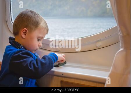 Süße kleine Kaukasischen Junge spielt auf dem Mobiltelefon während der Sitzung in der Fähre Beförderung Stockfoto