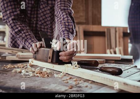 Tischler oder Schreiner mit einem alten Holz- Ebene die Oberfläche der Planken von Schnittholz in einem Holzbearbeitung Workshop zu glätten Stockfoto
