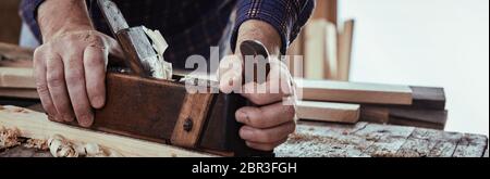 Panorama Banner eines Zimmermanns Hobeln Holz mit einem altmodischen hölzernen Flugzeug auf einem urigen Workbench in Nahaufnahme auf seinen Händen Stockfoto