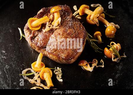 Dicke saftige Mariniertes gegrilltes Wild Steak mit Waldpilzen und Zwiebel in eine Schwarze Pfanne in Nahaufnahme hohen Winkel Stockfoto