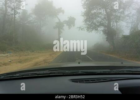 Blick auf eine Straße, umgeben von dichtem Nebel - wie durch die Windschutzscheibe eines Autos gesehen Stockfoto