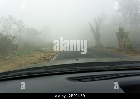 Blick auf eine Straße, umgeben von dichtem Nebel - wie durch die Windschutzscheibe eines Autos gesehen Stockfoto