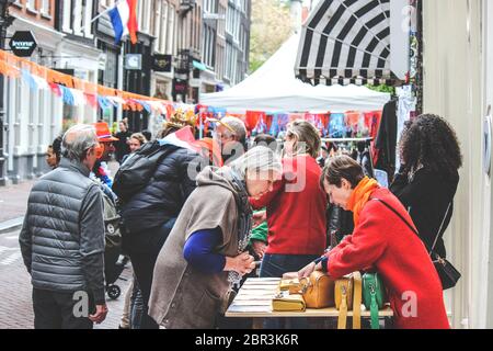 Amsterdam, Niederlande - 27. April 2019: Menschen kaufen und verkaufen auf dem traditionellen Flohmarkt während des Königstages, Koningsdag. Straßen mit holländischen Flaggen und Nationalfarben dekoriert. Stockfoto