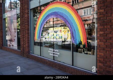 Ein Krankenwagen geht an einem Regenbogen im Schaufenster eines Ladens vorbei und dankt den Schlüsselarbeitern in einem verlassenen London während der Coronavirus-Pandemie in Großbritannien. Stockfoto