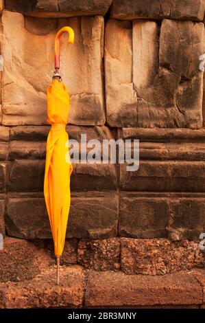 Gefalteter gelber Regenschirm lehnt sich an eine Wand. Roluos, Angkor, UNESCO-Weltkulturerbe, Provinz Siem Reap, Kambodscha, Südostasien Stockfoto
