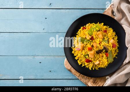 Gebratener Reis mit Huhn und Gemüse auf schwarzem Teller auf blauem Holztisch. Draufsicht. Kopierbereich Stockfoto