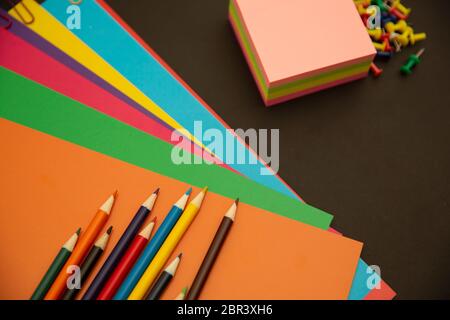 Bleistifte, mehrfarbiges Papier und Büroklammern auf schwarzem Hintergrund Stockfoto