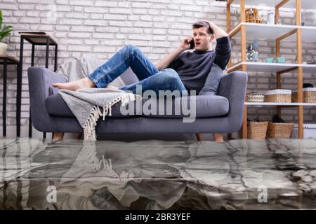 Überschwemmt von Wasser Leckage Vor Mann sitzt auf einem Sofa zu Klempner Stockfoto