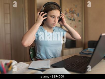 Teenager Mädchen 12-14 Jahre alt, setzt auf Kopfhörer nach Hause, Laptop-Unterricht, sieht Videos hört Musik. E-Education Fernstudium Internet-Video Stockfoto