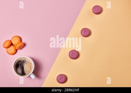 Stillleben mit einer Tasse Kaffee und köstlichen Makronen auf dem Hintergrund, bestehend aus zwei Farben rosa und gelb. Draufsicht mit Kopierbereich. Design Stockfoto