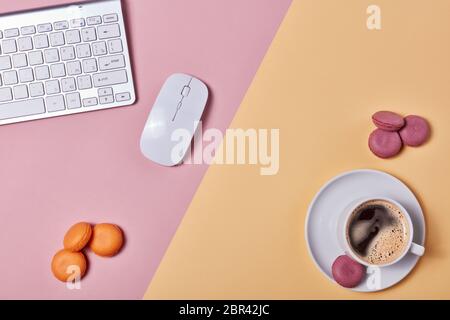 Tasse Kaffee, Makronen, Computertastatur und Maus auf Hintergrund bestehend aus zwei Farben rosa und gelb. Draufsicht mit Kopierbereich. Design-Elemen Stockfoto