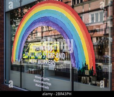 Ein Krankenwagen geht an einem Regenbogen im Schaufenster eines Ladens vorbei und dankt den Schlüsselarbeitern in einem verlassenen London während der Coronavirus-Pandemie in Großbritannien. Stockfoto