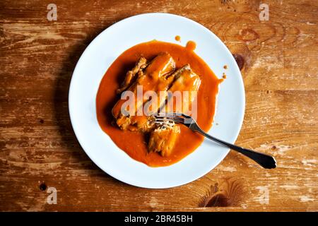 Ein weisser Porzellanteller mit Gabel und einem Fischfilet in Tomatensosse aus der Dose. Stockfoto