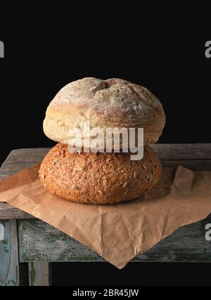 Zwei Brote gebacken runde Brot legen auf braunem Papier, schwarzer Hintergrund Stockfoto