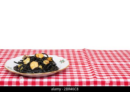 Tischplatte auf Meeresfrüchten Hintergrund. Nahaufnahme von mediterranen schwarzen Nudeln mit Tintenfischtinte, Muscheln und Garnelen auf einer rot karierten Tischdecke isolieren Stockfoto