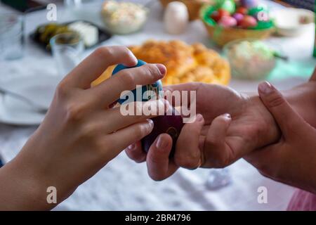 Klopfen Sie Eier auf ortodox Ostern mit einem Tisch voller Essen im Hintergrund Stockfoto