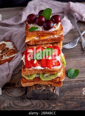 Stapel der French Toast von Weißbrot mit Hüttenkäse, Erdbeeren, Kiwis, Kirschen auf einem grauen Holzbrett Stockfoto