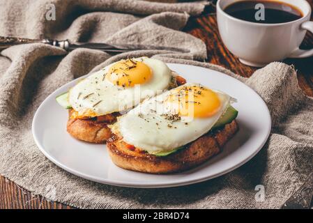 Toast mit Gemüse und Spiegeleier auf weißen Teller und Tasse Kaffee über Grau grobes Tuch. Stockfoto