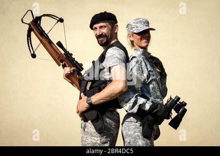 Die lächelnden Soldaten in Militäruniform posieren mit Armbrust und Fernglas. Stockfoto