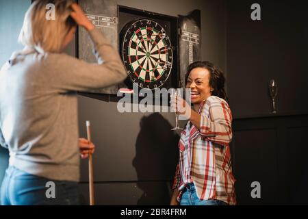 Zwei weibliche Freunde entspannen und Spaß haben. Sie stehen in einem Spielzimmer neben eine Dartscheibe, einen Drink. Stockfoto