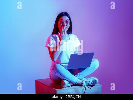 Moderne Blogger mit Laptop im Arbeitsbereich. Überraschte Mädchen in Brille schließt Mund mit der Hand Stockfoto