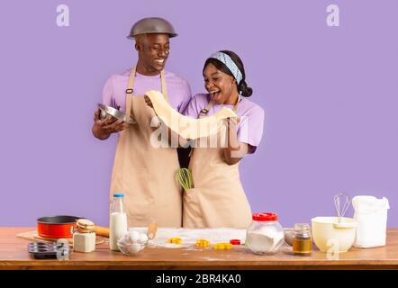 Romantische Kochzeiten. Junge schwarze Paar mit Teig Backen auf lila Hintergrund Stockfoto