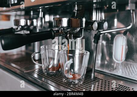 Duftender Espresso fließt aus einer Kaffeemaschine in eine Tasse. Aromatischer Kaffee mit professioneller Kaffeemaausrüstung zubereiten Stockfoto