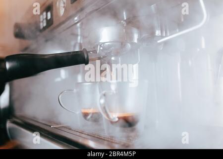 Duftender Espresso fließt aus einer Kaffeemaschine in eine Tasse. Aromatischer Kaffee mit professioneller Kaffeemaausrüstung zubereiten Stockfoto