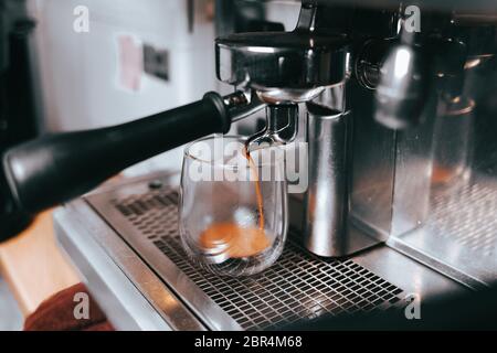 Duftender Espresso fließt aus einer Kaffeemaschine in eine Tasse. Aromatischer Kaffee mit professioneller Kaffeemaausrüstung zubereiten Stockfoto