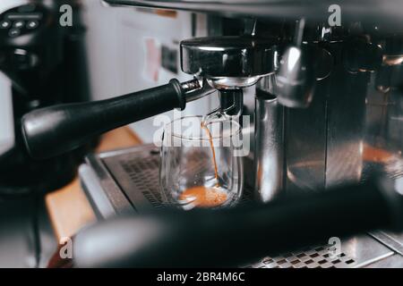 Duftender Espresso fließt aus einer Kaffeemaschine in eine Tasse. Aromatischer Kaffee mit professioneller Kaffeemaausrüstung zubereiten Stockfoto