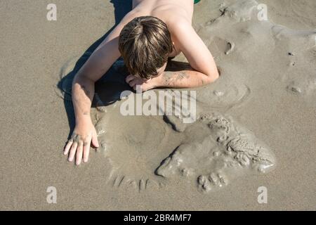 Junge macht Handabdrücke auf dem Sand am Strand Stockfoto