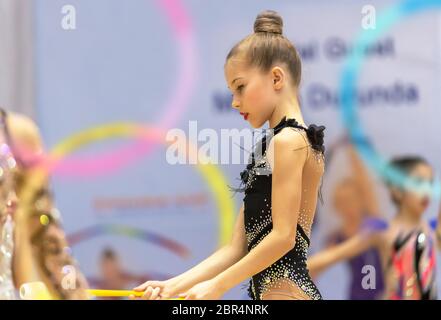 Schöne kleine Turnerin in der Wettbewerb in herrlichen schwarzen Leotard gekleidet führt eine akrobatische bewegt sich mit einer Hoop, rhythmische Gymnastik Schule Stockfoto