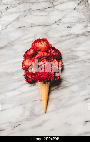 Flacher Eisbecher mit einer Kugel aus rot blühenden Ranunculus-Blüten auf weißem Marmortisch. Saisonaler Frühling oder Sommer natürlich Stockfoto