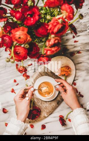 Flache Lage von Frauen Hand halten Tasse schwarzen Espresso Kaffee und Bouquet von roten Ranunculus Blumen über Servierbrett und weißen Marmortisch backgroun Stockfoto