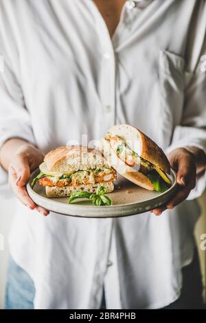 Frau in weißem Hemd mit Teller mit frischem gebratenem Fisch Sandwich mit Tartaresauce, Zitrone und Rucola in Hälften geschnitten, selektive Fokus. Gesund einfach b Stockfoto