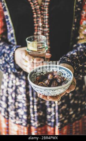 Frau in orientalischem Kleid hält Schüssel mit Datteln und frischem Trinkwasser in den Händen für Ramadan iftar Abendessen und Fastenmonat. Ramazan Muslim fasti Stockfoto