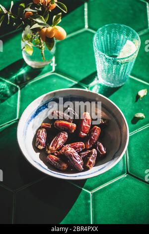 Traditionelle islamische Ramadan oder Ramazan Iftar Essen. Datteln in Schüssel und frisches Trinkwasser mit Zitrone in Glas über grünen orientalischen Fliesen Hintergrund, sel Stockfoto
