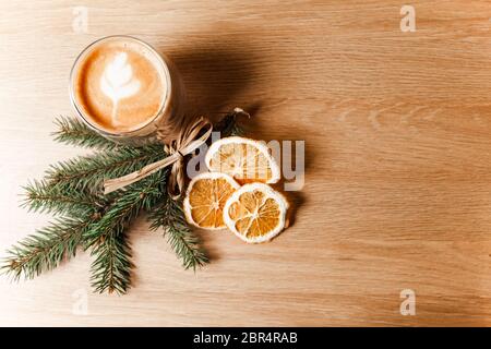 Zusammensetzung aus einer Tasse Latte, Kaffeebohnen, getrockneten Orangen und einem Tannenzweig. Stockfoto