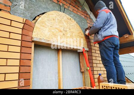 Der Meister in einem blauen Overall baut eine Wand aus Backstein.2020 Stockfoto