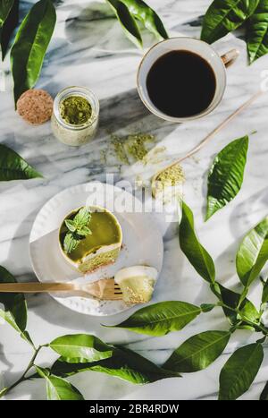 Kaffee und Dessert. Flaches Lay aus grünem Matcha-Käsekuchen und schwarzem Kaffee in Tasse über grauem Marmortisch Hintergrund, Draufsicht. Gesund, vegan, vegetarisch Stockfoto