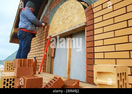 Der Meister in einem blauen Overall baut eine Wand aus Backstein.2020 Stockfoto